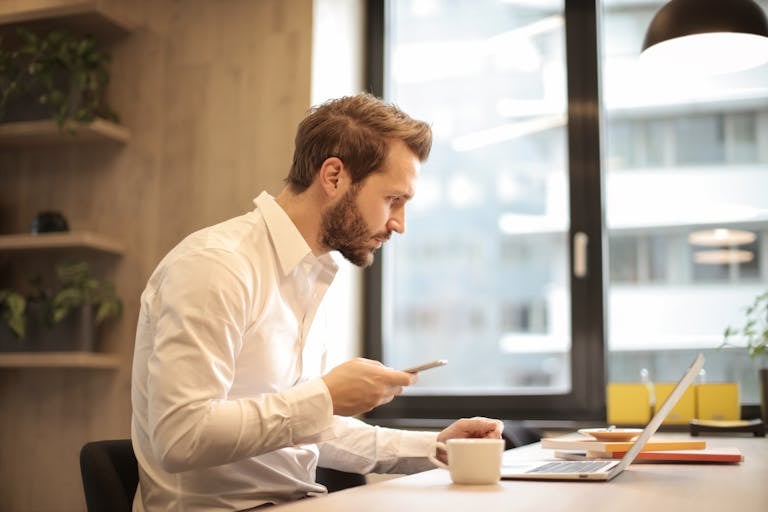 Homme d'affaires concentré travaillant sur son ordinateur portable tout en consultant son smartphone dans un bureau moderne. Homme d'affaires concentré travaillant sur son ordinateur portable tout en consultant son smartphone dans un bureau moderne. Homme d'affaires concentré travaillant sur son ordinateur portable tout en consultant son smartphone dans un bureau moderne.